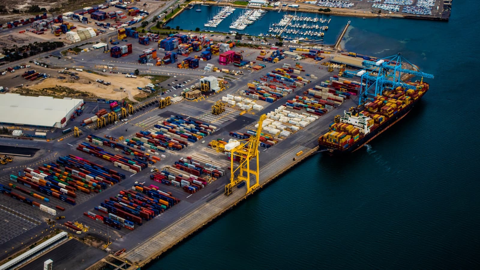 A cargo vessel berthed beside stacked containers, seen from above